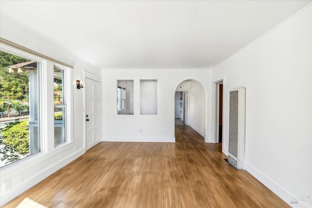 empty room featuring light wood-type flooring, arched walkways, baseboards, and a heating unit