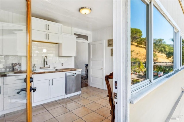 kitchen featuring light tile patterned floors, decorative backsplash, stainless steel dishwasher, white cabinets, and a sink