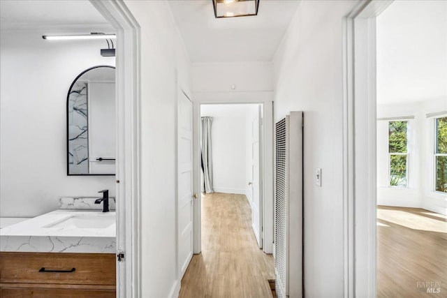 corridor featuring a heating unit, crown molding, baseboards, light wood-style flooring, and a sink
