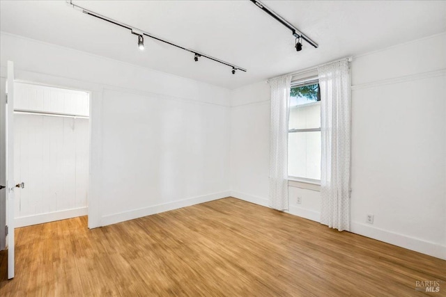 unfurnished bedroom with rail lighting, baseboards, and wood finished floors