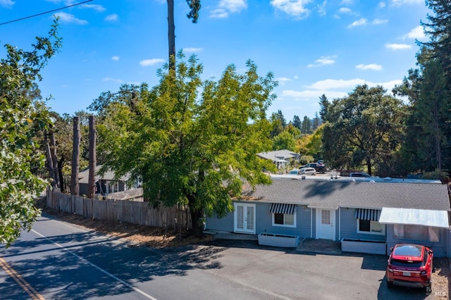 view of front of house with french doors, a shingled roof, and fence