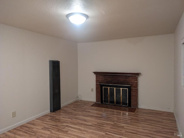 unfurnished living room featuring a textured ceiling, a brick fireplace, and wood-type flooring