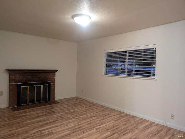 unfurnished living room featuring wood-type flooring, a textured ceiling, and a brick fireplace