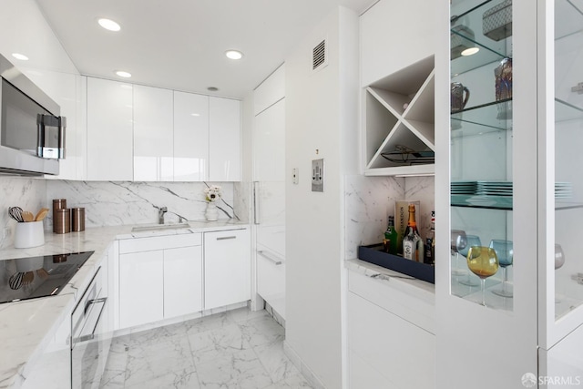 kitchen with black electric stovetop, backsplash, sink, light stone countertops, and white cabinets