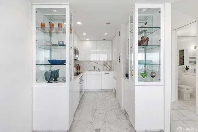 bar featuring sink, white cabinets, stainless steel appliances, and backsplash