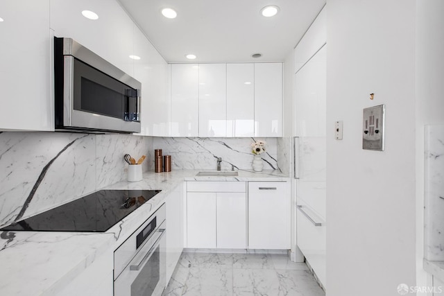 kitchen with sink, white cabinetry, stainless steel appliances, light stone counters, and decorative backsplash