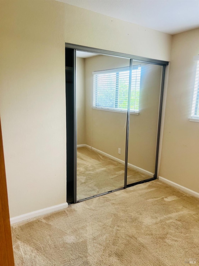 unfurnished bedroom with multiple windows, a closet, and light colored carpet