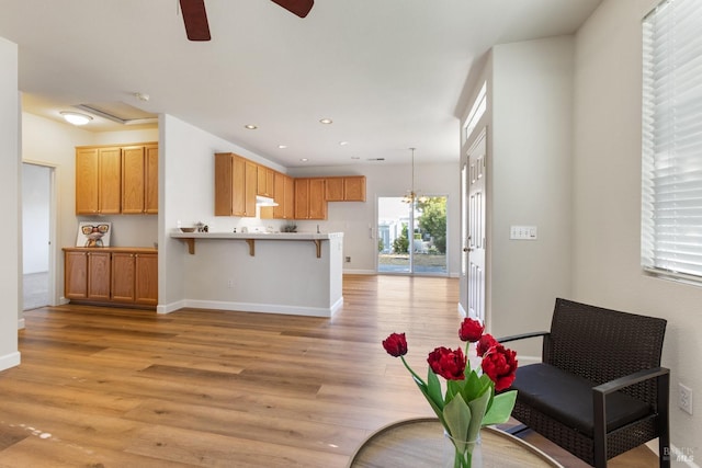 interior space with hanging light fixtures, light hardwood / wood-style flooring, ceiling fan, kitchen peninsula, and a breakfast bar area