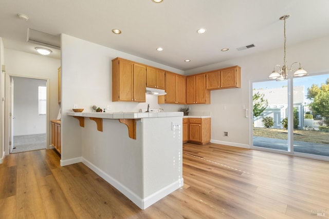 kitchen with pendant lighting, light wood-type flooring, kitchen peninsula, and an inviting chandelier