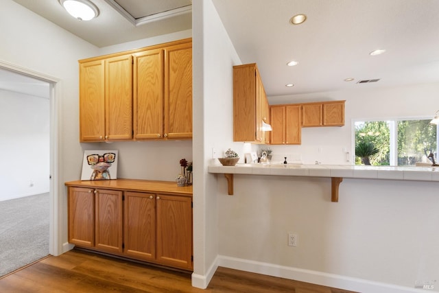 kitchen with tile counters, dark hardwood / wood-style floors, and a breakfast bar