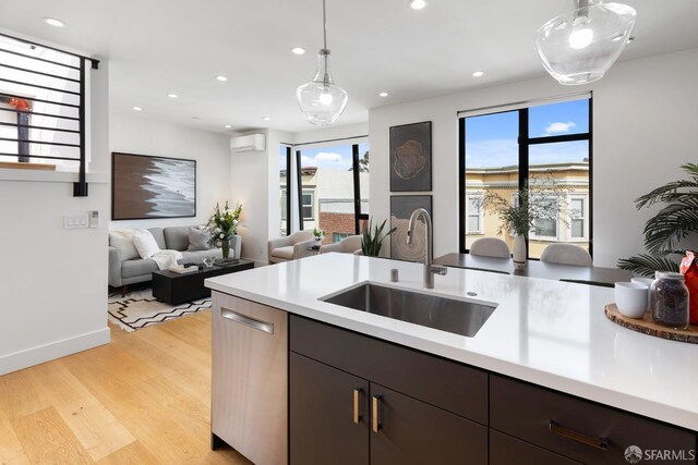 kitchen with sink, hanging light fixtures, stainless steel dishwasher, a wall unit AC, and light hardwood / wood-style floors