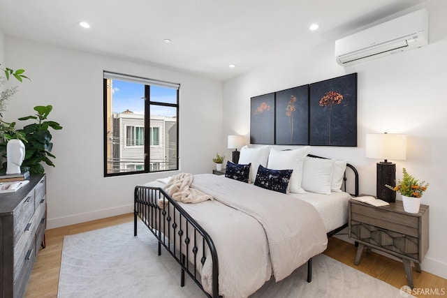 bedroom with a wall mounted AC and light hardwood / wood-style floors