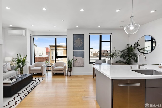 kitchen with sink, a wall mounted air conditioner, hanging light fixtures, light wood-type flooring, and an island with sink