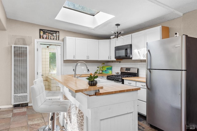 kitchen featuring lofted ceiling with skylight, a kitchen island, appliances with stainless steel finishes, butcher block countertops, and white cabinets