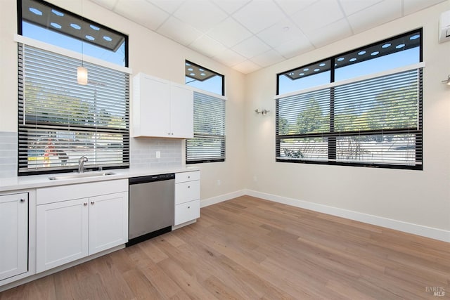 kitchen with a wealth of natural light, stainless steel dishwasher, white cabinets, sink, and hanging light fixtures