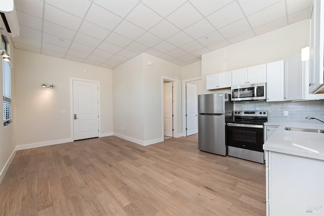 kitchen featuring light wood-type flooring, sink, an AC wall unit, white cabinets, and appliances with stainless steel finishes