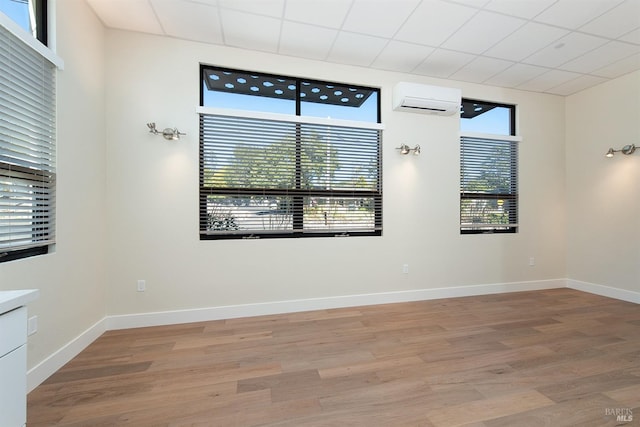 empty room with wood-type flooring, a paneled ceiling, and a wall mounted AC