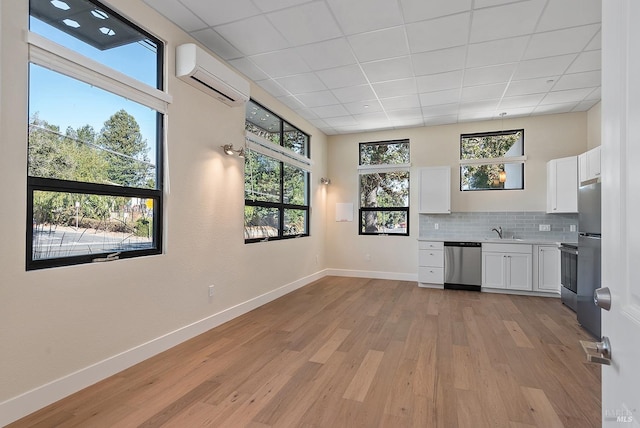 kitchen featuring appliances with stainless steel finishes, plenty of natural light, an AC wall unit, and white cabinets