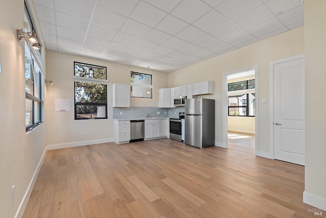 kitchen with stainless steel appliances, light hardwood / wood-style floors, white cabinets, and a healthy amount of sunlight