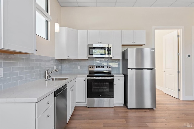 kitchen with appliances with stainless steel finishes, a drop ceiling, white cabinetry, and sink