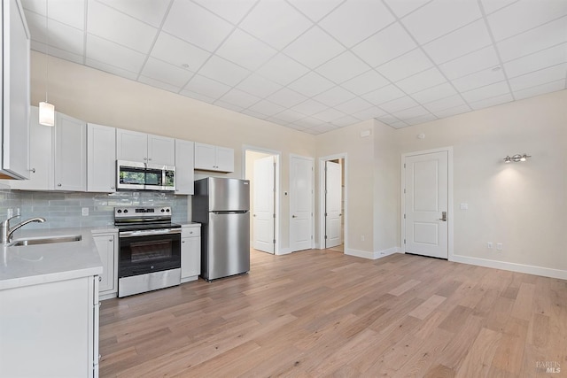 kitchen with white cabinets, sink, decorative light fixtures, appliances with stainless steel finishes, and light wood-type flooring