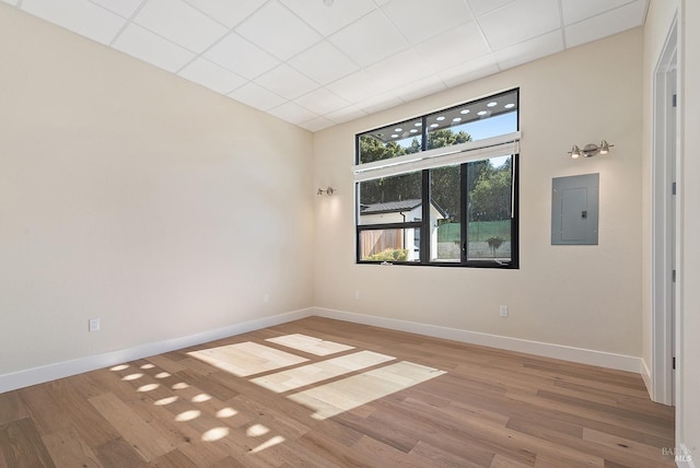 unfurnished room with wood-type flooring, electric panel, and a drop ceiling