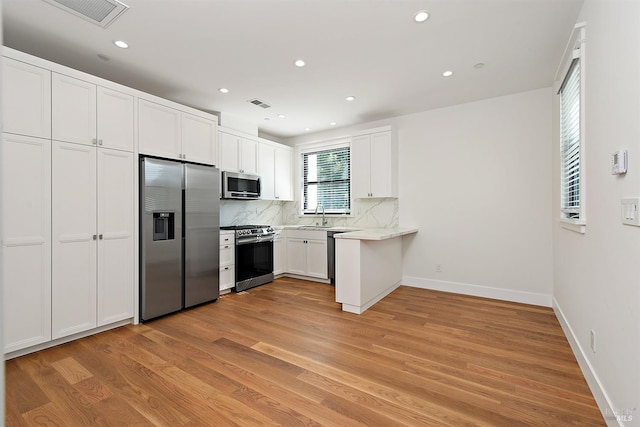 kitchen featuring light wood-type flooring, decorative backsplash, stainless steel appliances, white cabinets, and sink