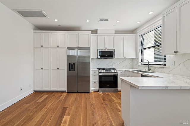 kitchen featuring light wood-type flooring, tasteful backsplash, sink, white cabinets, and appliances with stainless steel finishes