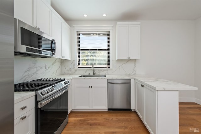 kitchen with sink, kitchen peninsula, appliances with stainless steel finishes, hardwood / wood-style flooring, and white cabinetry