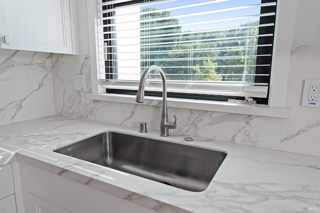 details featuring decorative backsplash, white cabinets, sink, and light stone counters