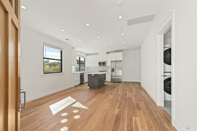 kitchen with a center island, stainless steel appliances, light hardwood / wood-style floors, white cabinetry, and stacked washer / drying machine