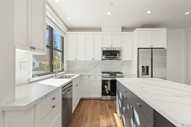 kitchen featuring wood-type flooring, sink, stainless steel appliances, light stone countertops, and white cabinetry