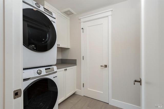 clothes washing area with light tile patterned flooring, stacked washer / dryer, and cabinets