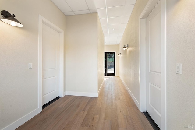 hallway with light wood-type flooring and a drop ceiling