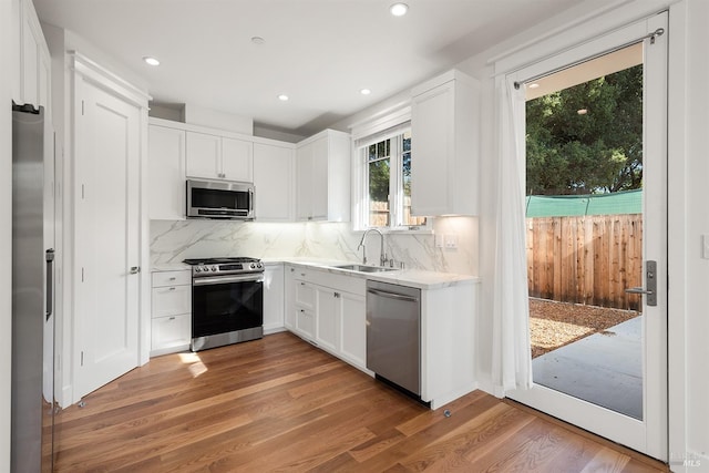 kitchen featuring decorative backsplash, hardwood / wood-style floors, sink, stainless steel appliances, and white cabinetry