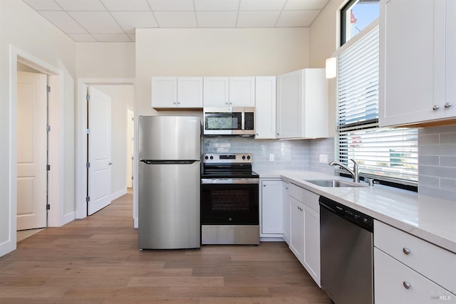 kitchen with light hardwood / wood-style floors, a paneled ceiling, sink, stainless steel appliances, and white cabinets