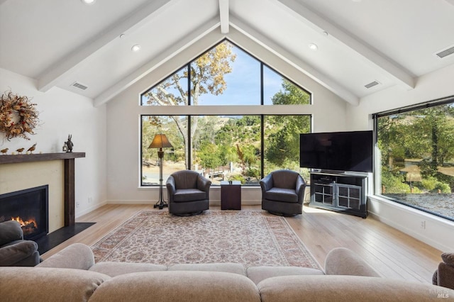 living room featuring vaulted ceiling with beams, light wood-type flooring, and a wealth of natural light