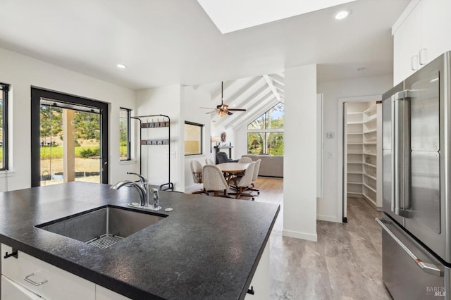 kitchen with light wood-type flooring, high quality fridge, sink, a center island with sink, and white cabinets