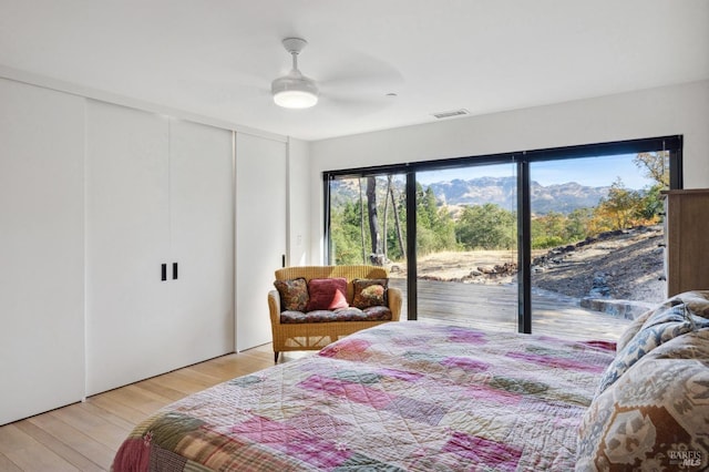 bedroom with access to exterior, a mountain view, light wood-type flooring, and ceiling fan