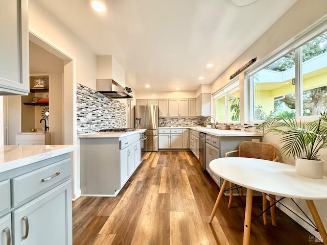 kitchen with backsplash, stainless steel appliances, wall chimney range hood, and light hardwood / wood-style floors