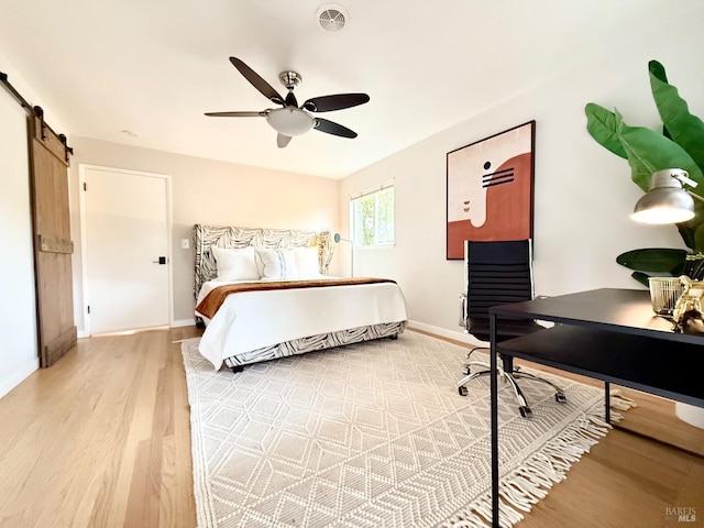 bedroom with hardwood / wood-style floors, ceiling fan, and a barn door