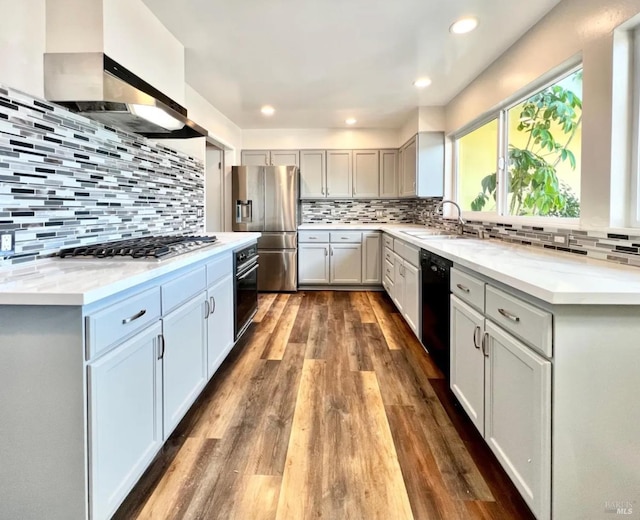 kitchen with light stone countertops, sink, wall chimney range hood, and black appliances