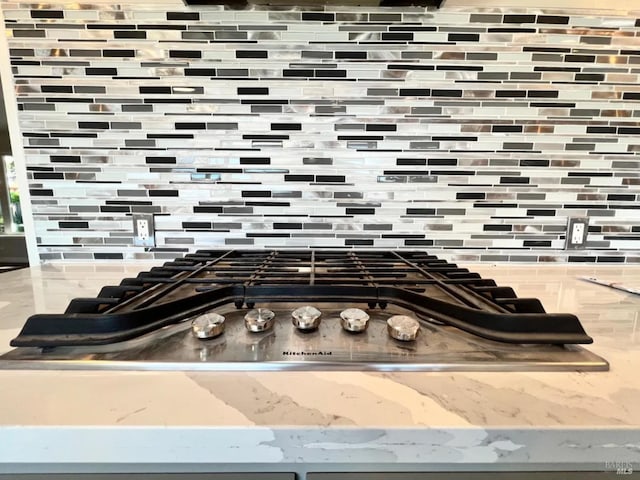 interior details featuring light stone countertops, backsplash, and stainless steel gas cooktop