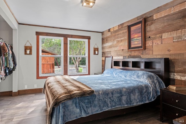 bedroom featuring wood-type flooring, wooden walls, crown molding, and a fireplace