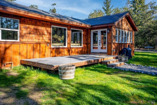 rear view of property featuring french doors, a wooden deck, and a lawn