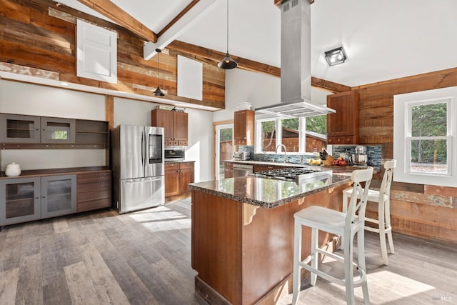 kitchen featuring island range hood, dark stone countertops, light wood-type flooring, appliances with stainless steel finishes, and beam ceiling