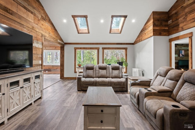 living room with a skylight, high vaulted ceiling, wood walls, and light wood-type flooring