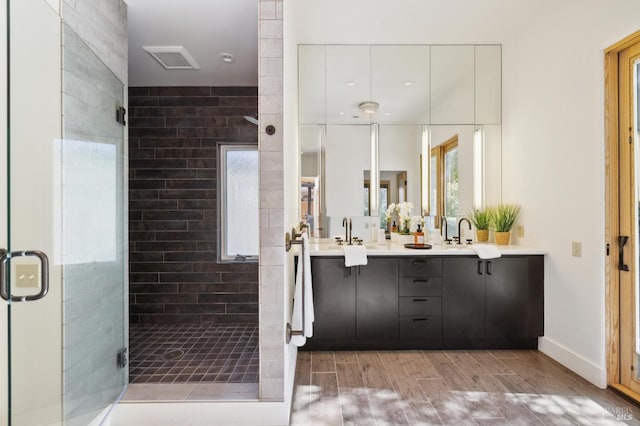 bathroom featuring visible vents, a shower stall, double vanity, wood finished floors, and a sink