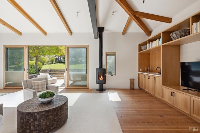 living area featuring a wood stove, light wood-style floors, and beamed ceiling