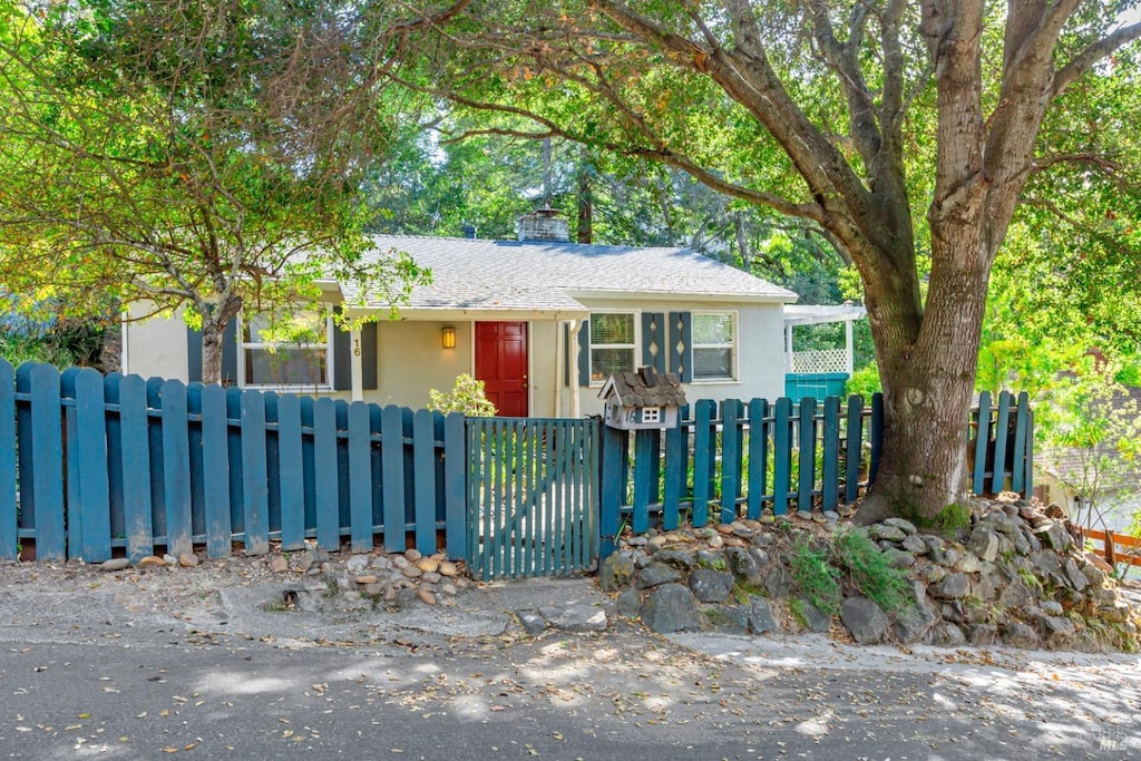 ranch-style home featuring stucco siding, a chimney, and a fenced front yard